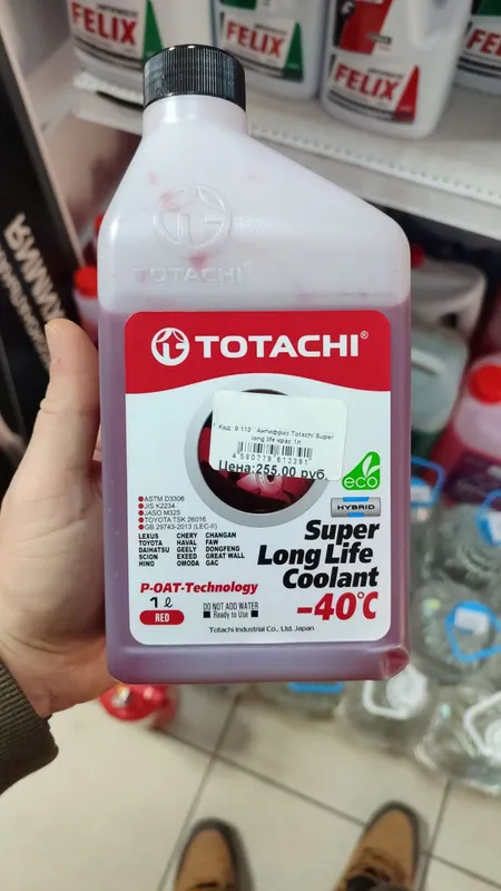 Литровая бутылка красного Totachi Super Long Life Coolant на -40 в руке у полки магазина, на этикетке P-OAT, JIS K2234 и допуск Toyota