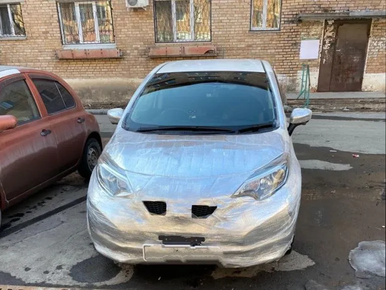 Ниссан Ноут во дворе, вся передняя часть затянута фольгированным утеплителем, открыты только два узких отверстия в бампере